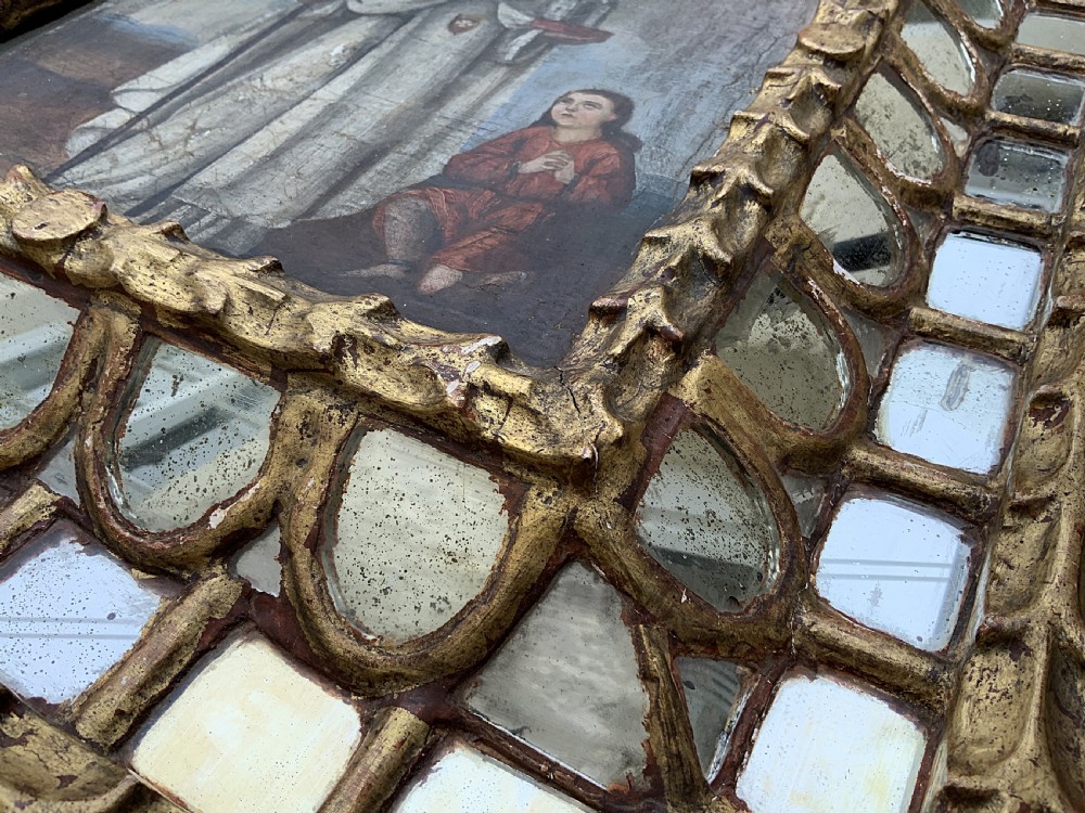 A 17th-century Spanish Baroque oil painting depicting a saint in a habit holding a banner alongside a kneeling figure, housed within an ornate carved giltwood lattice frame with mirrored glass inserts. View XI