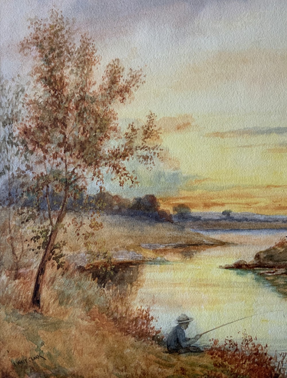 Framed antique watercolour painting depicting a figure fishing along a riverbank at sunset beside trees and cottages. View V