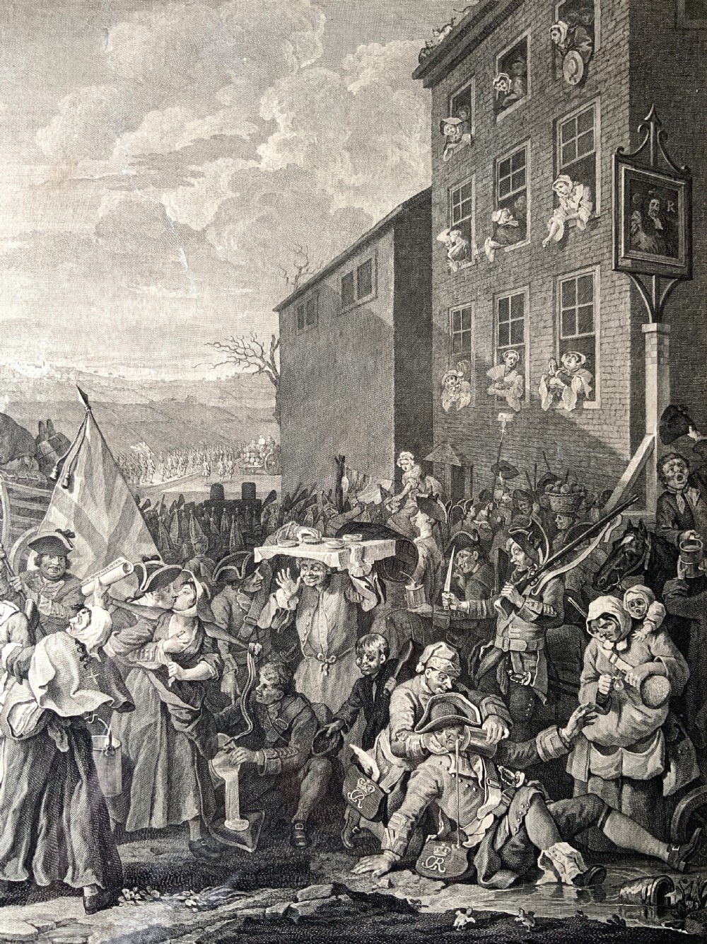 An 18th-century black and white satirical engraving depicting a crowded street scene with soldiers, housed in a black and gold frame with a cream mount. View VII