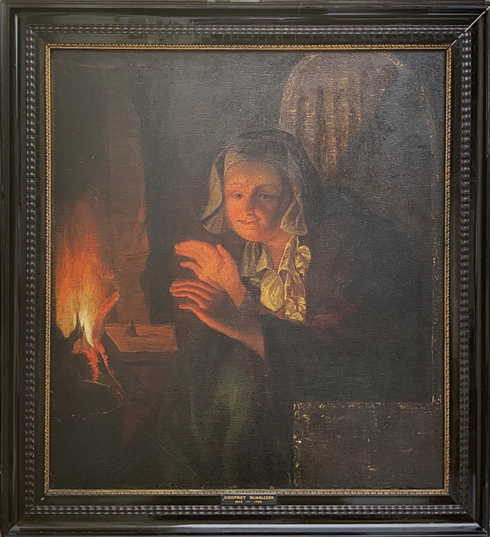 A framed oil painting depicting a woman in historic dress warming her hands beside a glowing fire in a darkened interior.