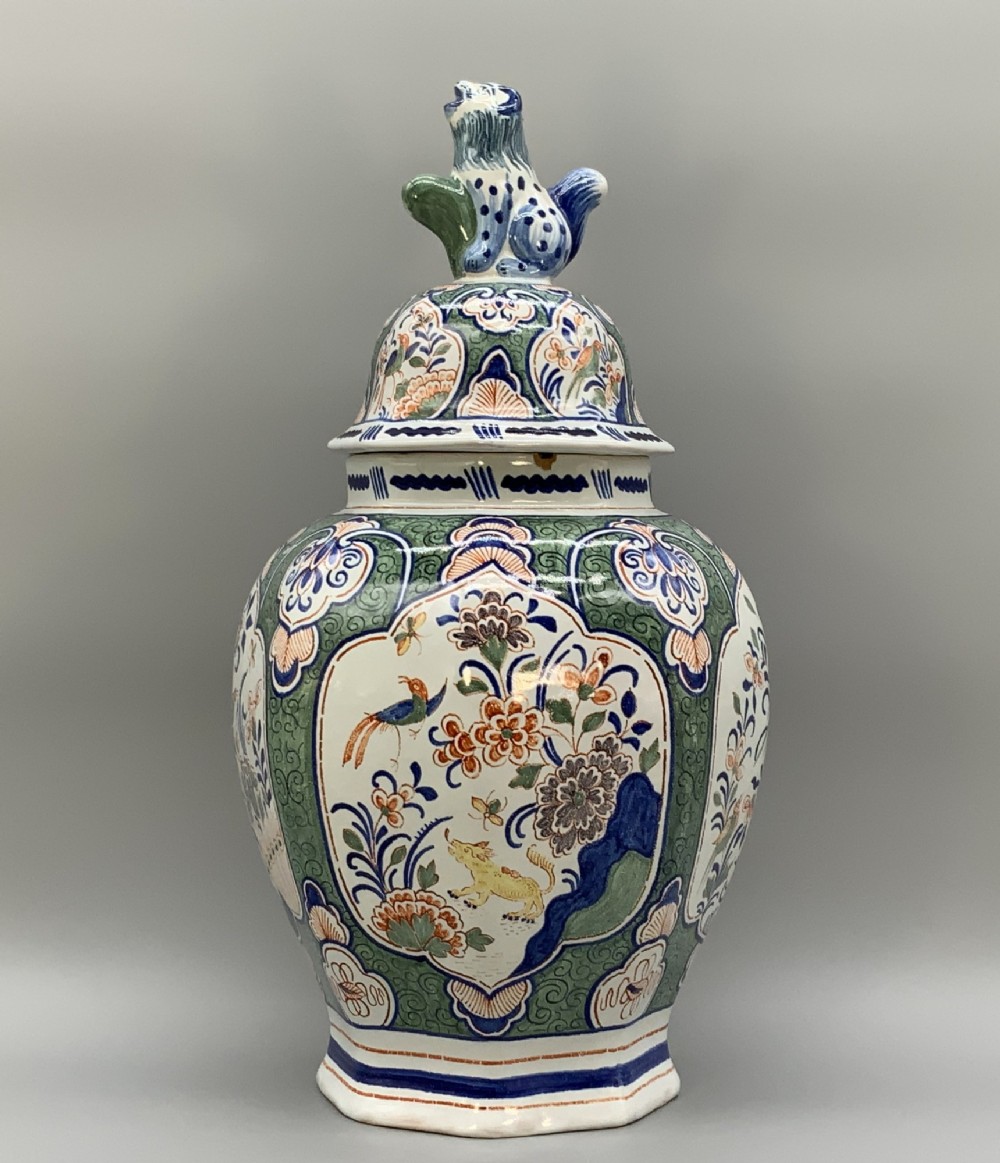 An octagonal tin-glazed ceramic baluster vase with a matching cover topped by a sculpted lion finial and decorated with multi-coloured floral panels.