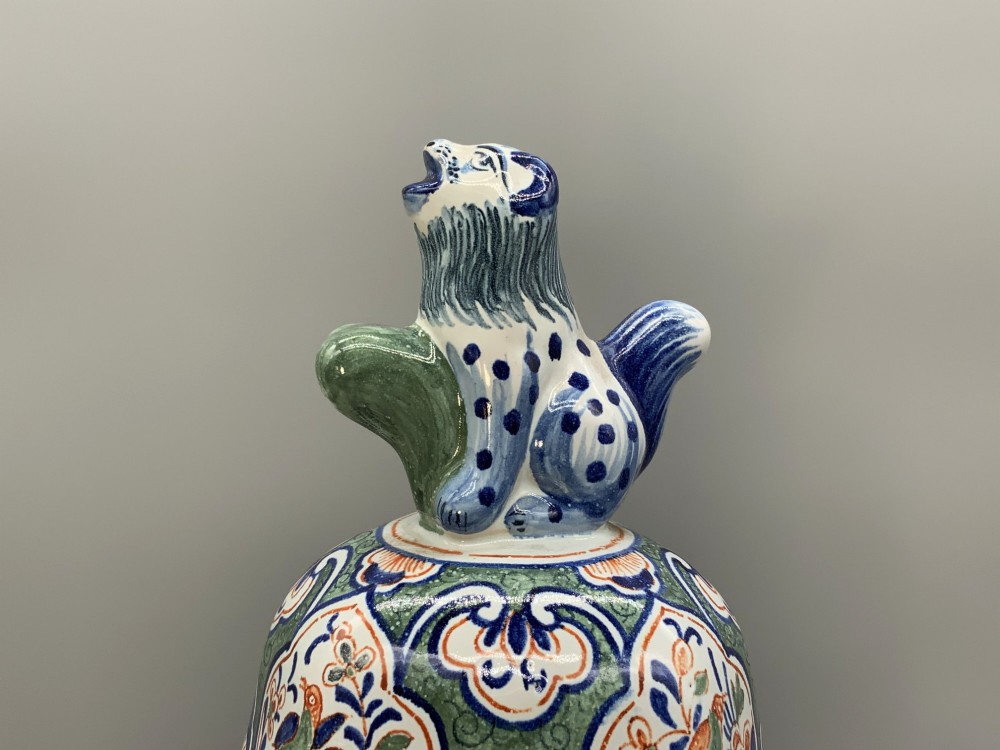 An octagonal tin-glazed ceramic baluster vase with a matching cover topped by a sculpted lion finial and decorated with multi-coloured floral panels. View IV