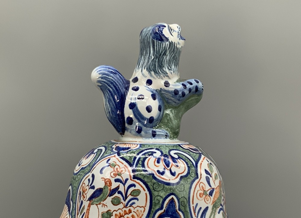 An octagonal tin-glazed ceramic baluster vase with a matching cover topped by a sculpted lion finial and decorated with multi-coloured floral panels. View IX
