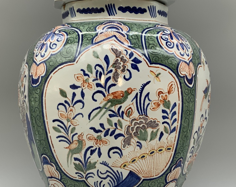 An octagonal tin-glazed ceramic baluster vase with a matching cover topped by a sculpted lion finial and decorated with multi-coloured floral panels. View X