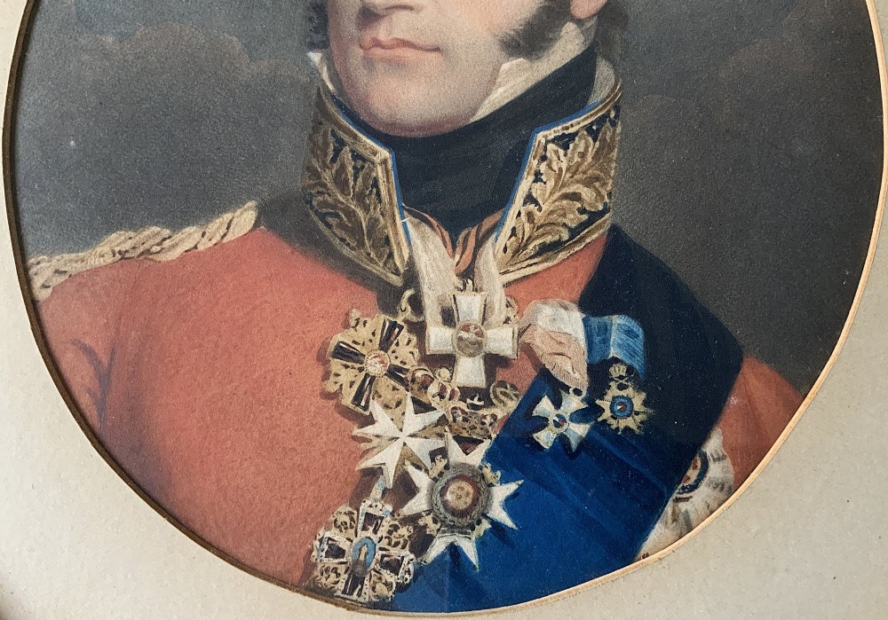 A circular gilt-framed miniature portrait print depicting a man in a red military uniform with medals and a blue sash. View VI