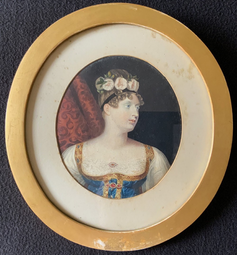 A circular gilt-framed hand-coloured miniature portrait depicting a young woman wearing a floral headband and blue dress.
