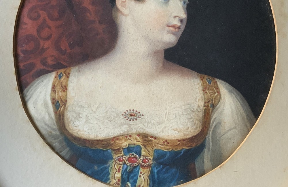 A circular gilt-framed hand-coloured miniature portrait depicting a young woman wearing a floral headband and blue dress. View VI