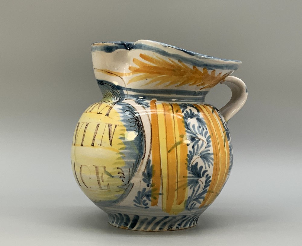 An antique Italian majolica earthenware pharmacy jug with hand-painted yellow, blue, and manganese script reading CARA BEVI IN PACE. View IV