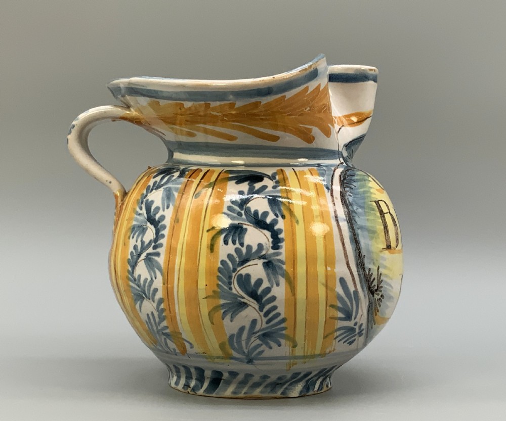 An antique Italian majolica earthenware pharmacy jug with hand-painted yellow, blue, and manganese script reading CARA BEVI IN PACE. View VIII