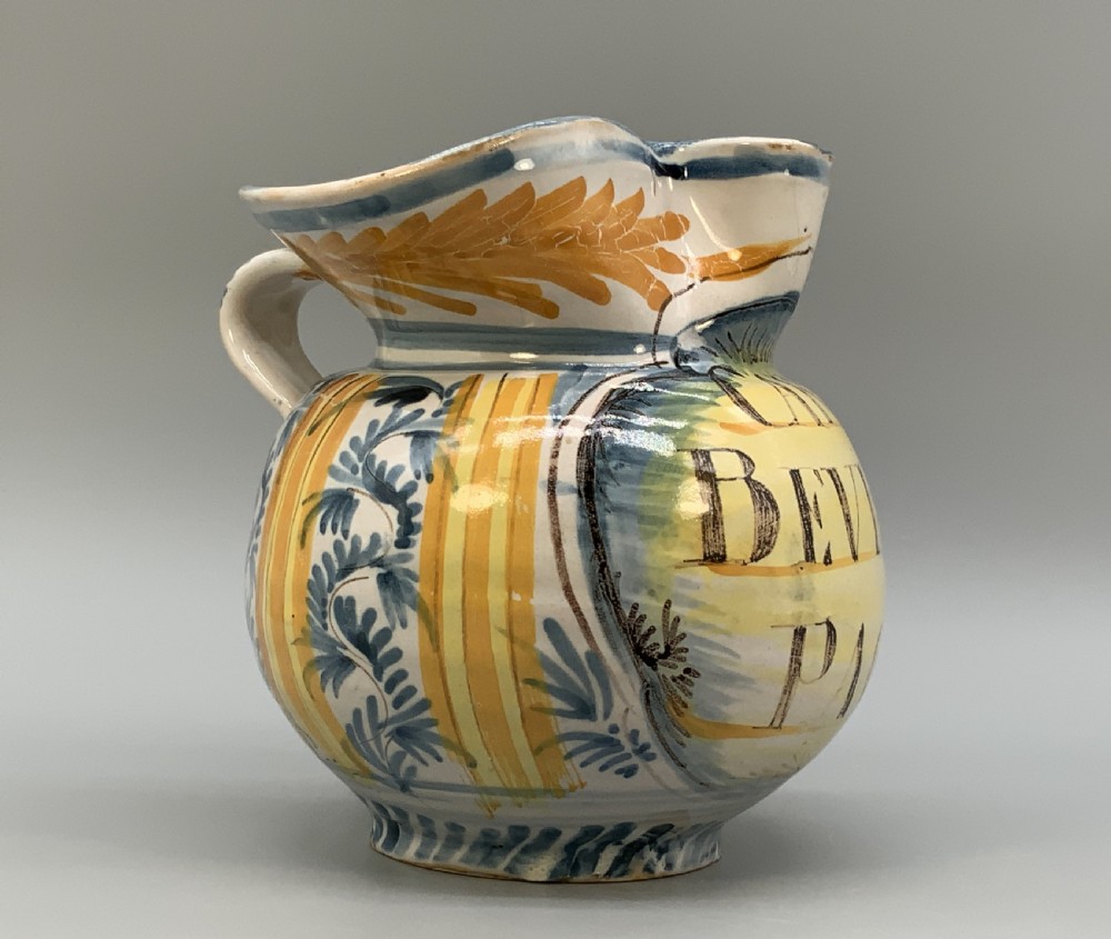 An antique Italian majolica earthenware pharmacy jug with hand-painted yellow, blue, and manganese script reading CARA BEVI IN PACE. View IX