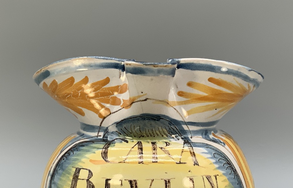 An antique Italian majolica earthenware pharmacy jug with hand-painted yellow, blue, and manganese script reading CARA BEVI IN PACE. View XI