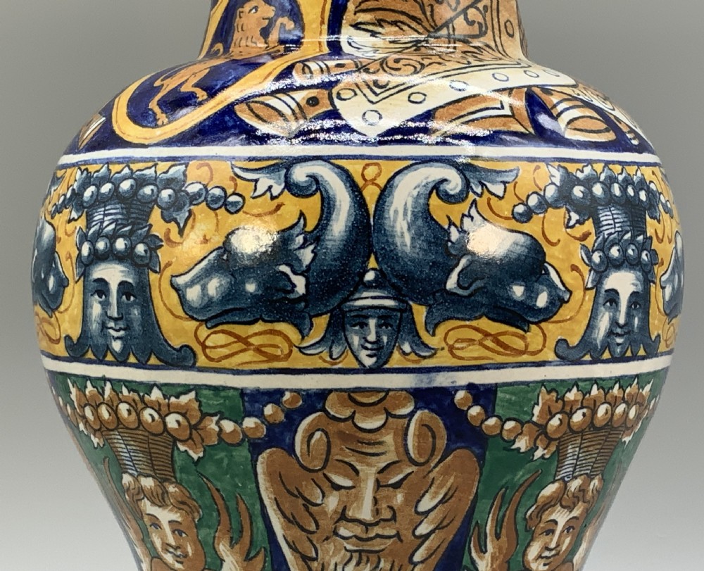 A tall hand-painted polychrome majolica ceramic vase featuring classical faces, winged cherub figures, and scrolling foliage on a circular pedestal foot. View VII
