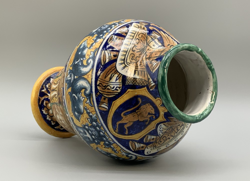 A tall hand-painted polychrome majolica ceramic vase featuring classical faces, winged cherub figures, and scrolling foliage on a circular pedestal foot. View XI