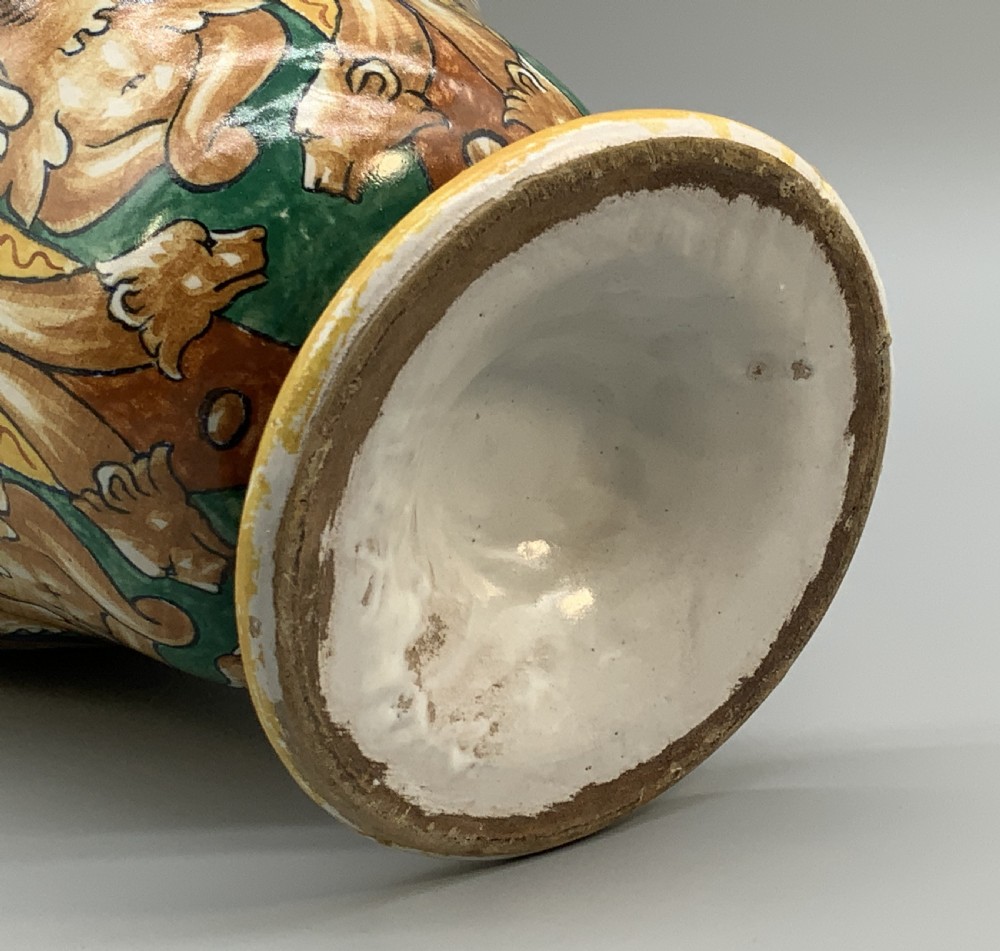 A tall hand-painted polychrome majolica ceramic vase featuring classical faces, winged cherub figures, and scrolling foliage on a circular pedestal foot. View XIII