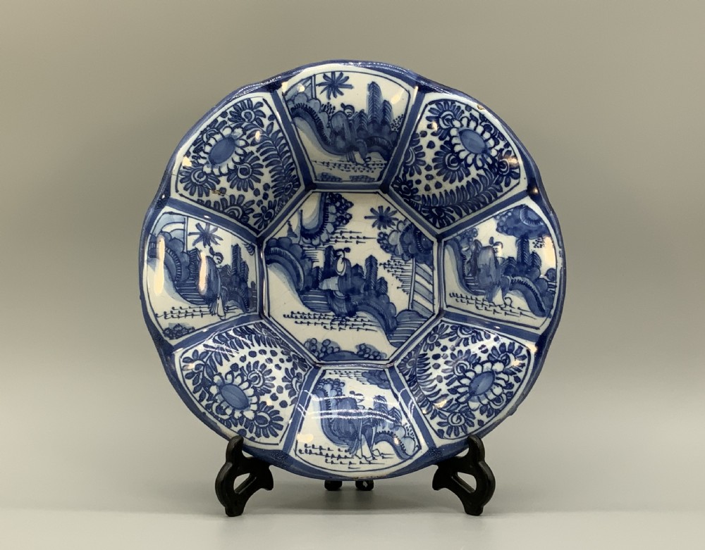 A blue and white tin-glazed earthenware lobed dish featuring panelled borders and a central Chinoiserie landscape scene.