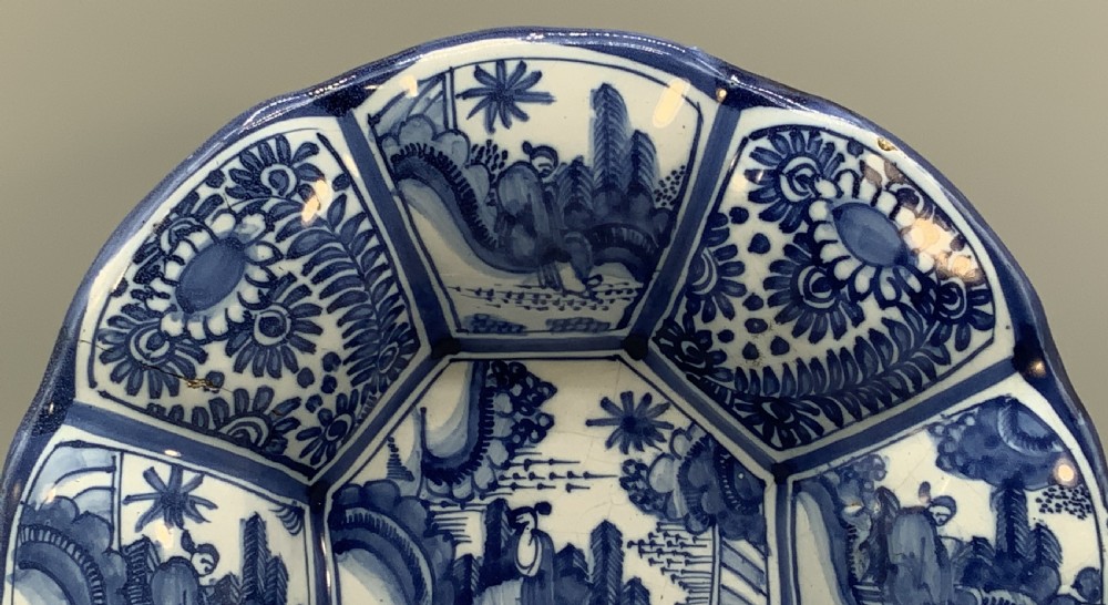 A blue and white tin-glazed earthenware lobed dish featuring panelled borders and a central Chinoiserie landscape scene. View V