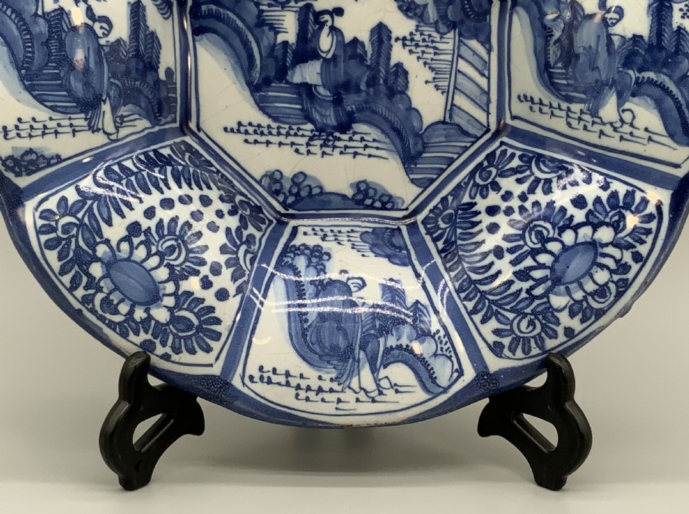 A blue and white tin-glazed earthenware lobed dish featuring panelled borders and a central Chinoiserie landscape scene. View VII