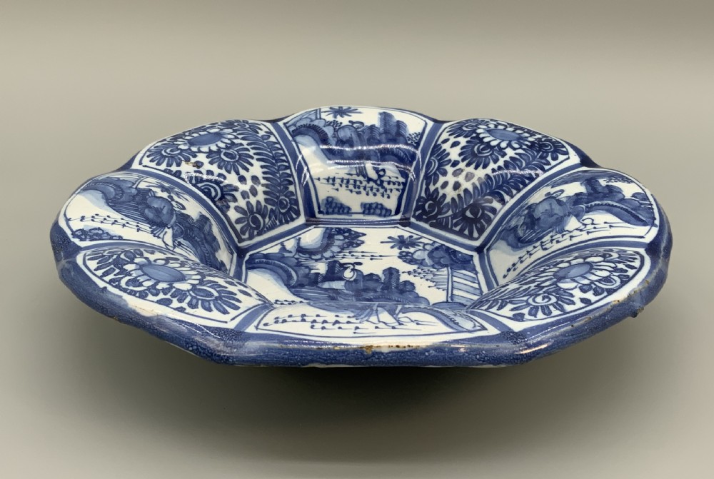 A blue and white tin-glazed earthenware lobed dish featuring panelled borders and a central Chinoiserie landscape scene. View XVI