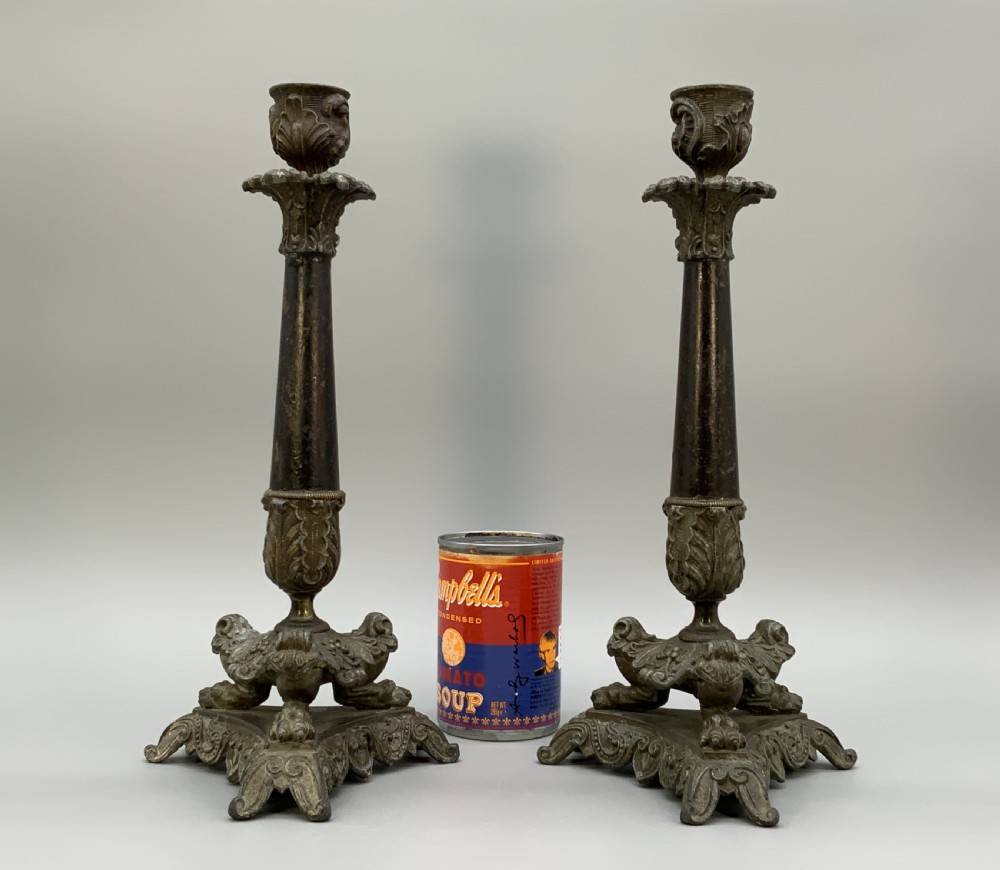 A pair of nineteenth-century French Empire metal candlesticks featuring dark tapered columns, ornate acanthus leaf capitals, and decorative triangular bases. View III