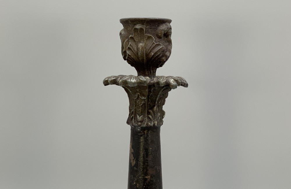A pair of nineteenth-century French Empire metal candlesticks featuring dark tapered columns, ornate acanthus leaf capitals, and decorative triangular bases. View IV
