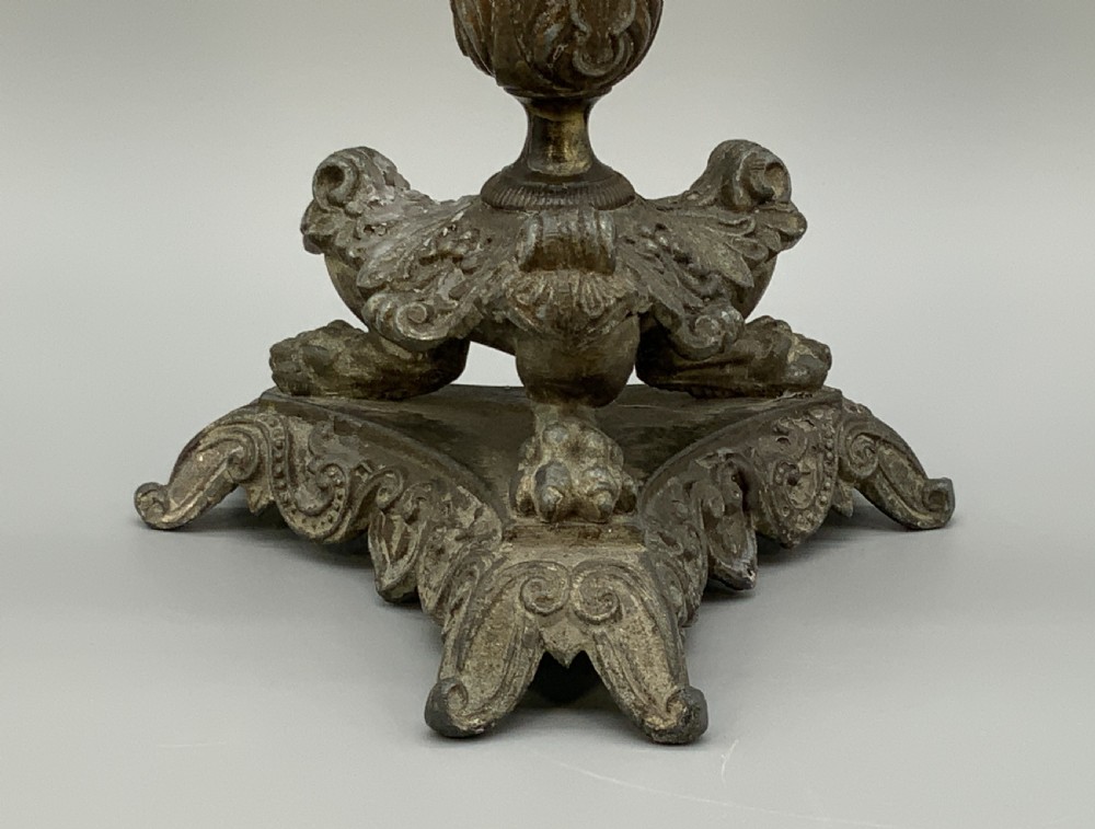 A pair of nineteenth-century French Empire metal candlesticks featuring dark tapered columns, ornate acanthus leaf capitals, and decorative triangular bases. View V