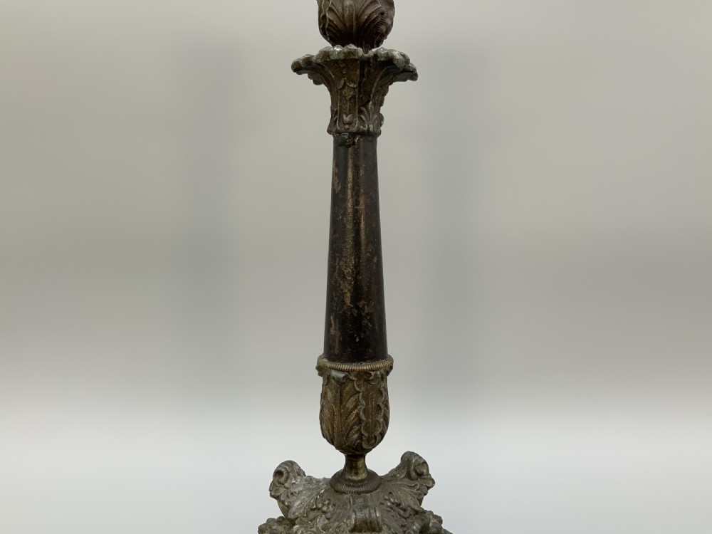 A pair of nineteenth-century French Empire metal candlesticks featuring dark tapered columns, ornate acanthus leaf capitals, and decorative triangular bases. View VIII