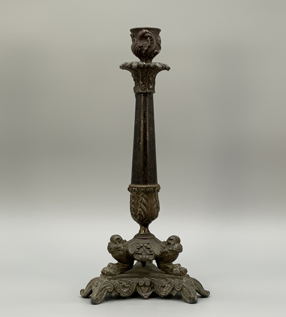 A pair of nineteenth-century French Empire metal candlesticks featuring dark tapered columns, ornate acanthus leaf capitals, and decorative triangular bases. View X