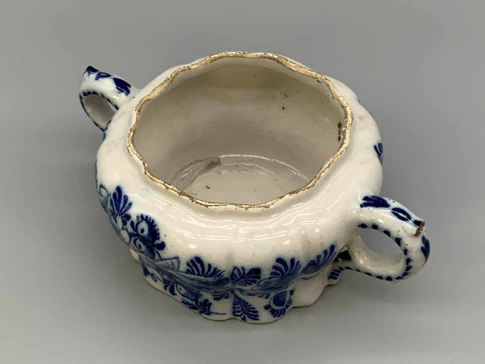 A 17th-century English Delftware lidded pot painted with cobalt blue floral motifs, featuring two side loop handles and a knopped lid. View X