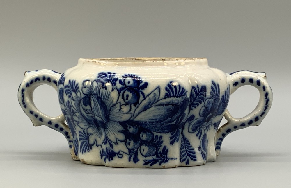 A 17th-century English Delftware lidded pot painted with cobalt blue floral motifs, featuring two side loop handles and a knopped lid. View XIV
