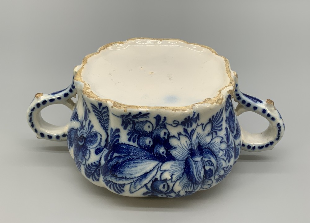 A 17th-century English Delftware lidded pot painted with cobalt blue floral motifs, featuring two side loop handles and a knopped lid. View XVII