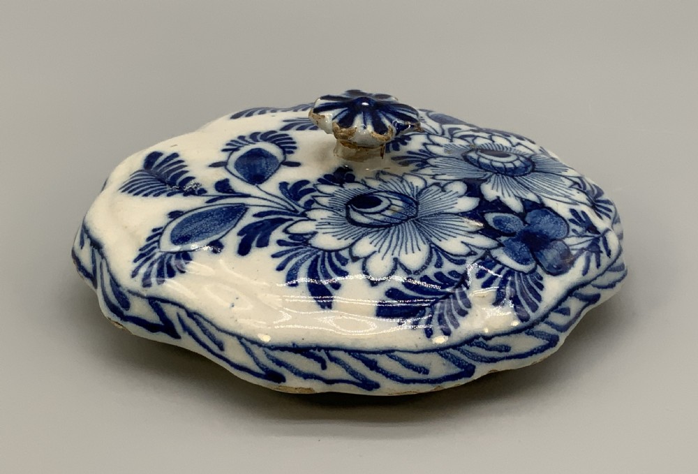 A 17th-century English Delftware lidded pot painted with cobalt blue floral motifs, featuring two side loop handles and a knopped lid. View XIX