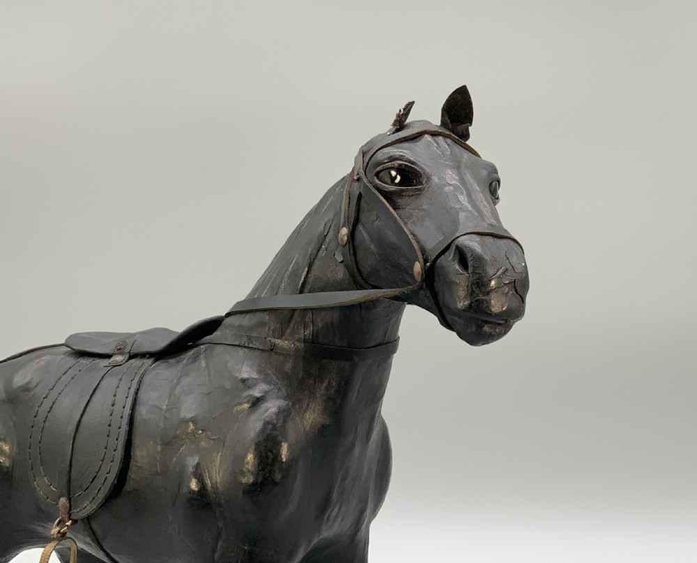 A standing vintage dark leather horse sculpture detailed with a miniature saddle, bridle, and metal stirrups. View IV