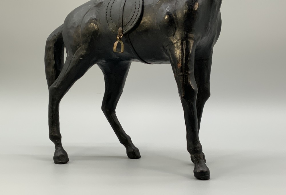 A standing vintage dark leather horse sculpture detailed with a miniature saddle, bridle, and metal stirrups. View VI
