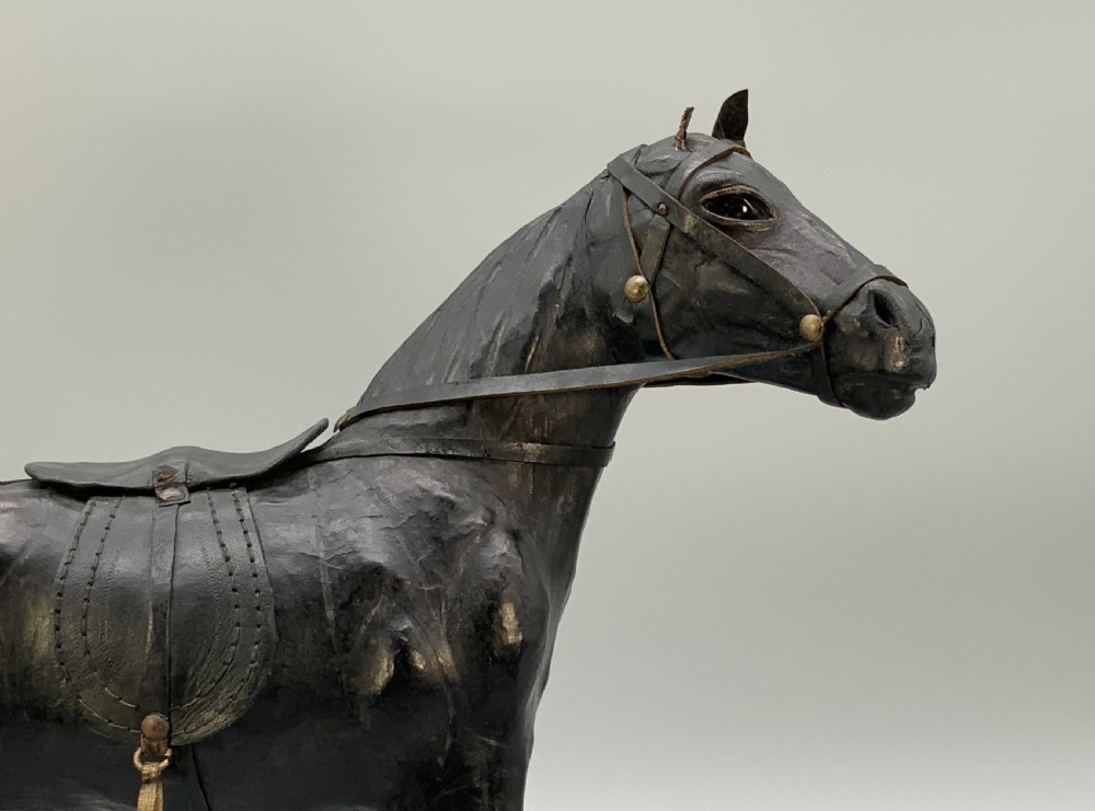 A standing vintage dark leather horse sculpture detailed with a miniature saddle, bridle, and metal stirrups. View VIII