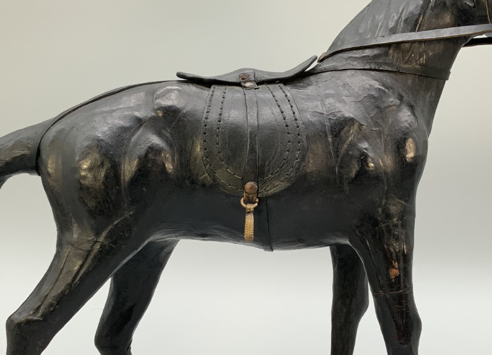 A standing vintage dark leather horse sculpture detailed with a miniature saddle, bridle, and metal stirrups. View IX