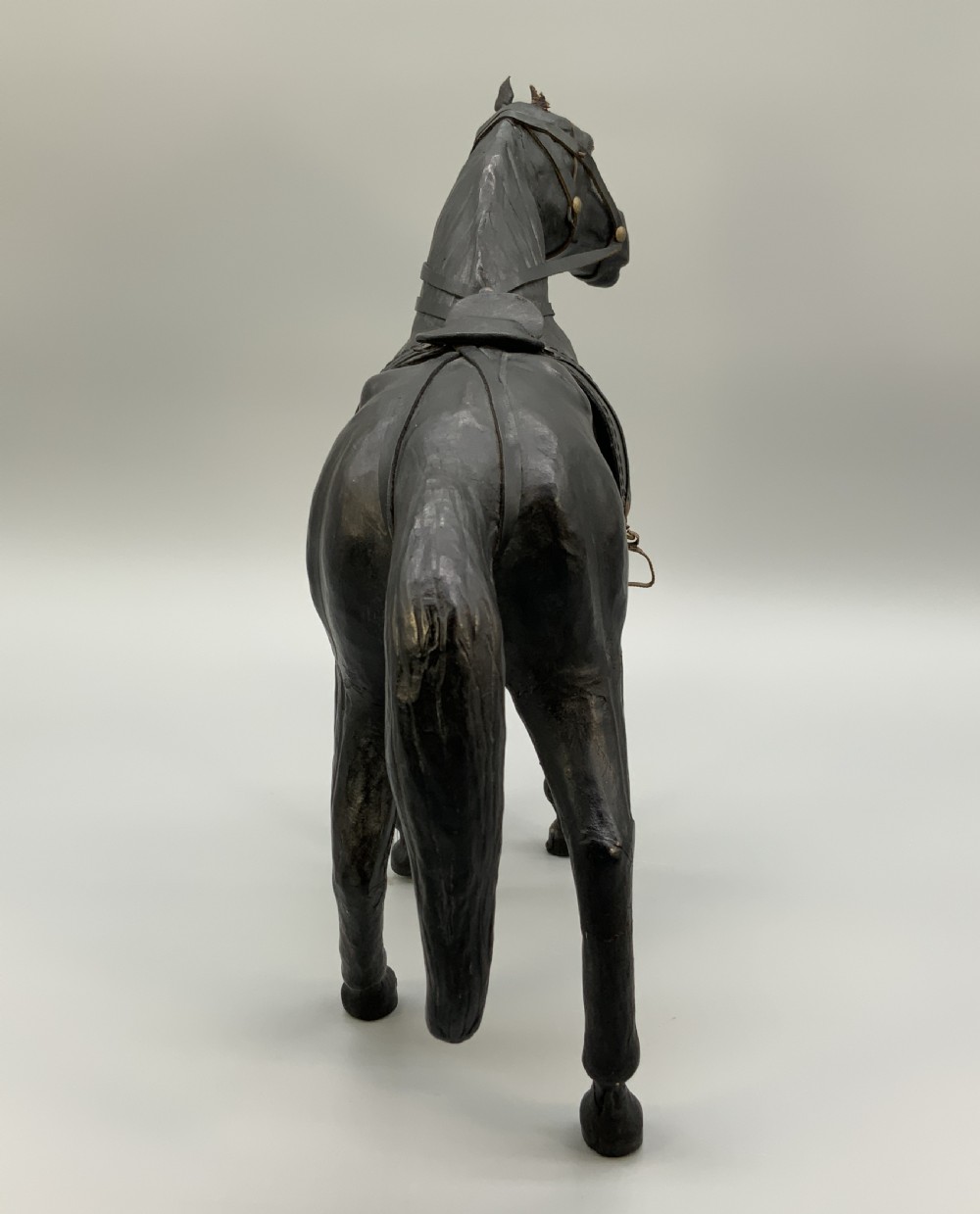 A standing vintage dark leather horse sculpture detailed with a miniature saddle, bridle, and metal stirrups. View XIV