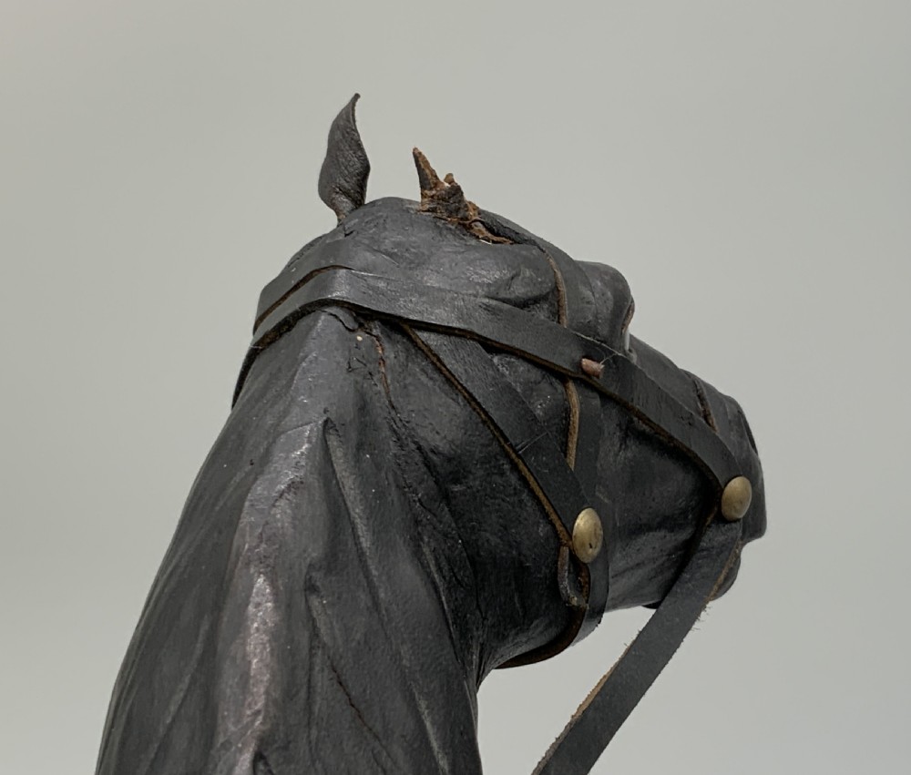A standing vintage dark leather horse sculpture detailed with a miniature saddle, bridle, and metal stirrups. View XV