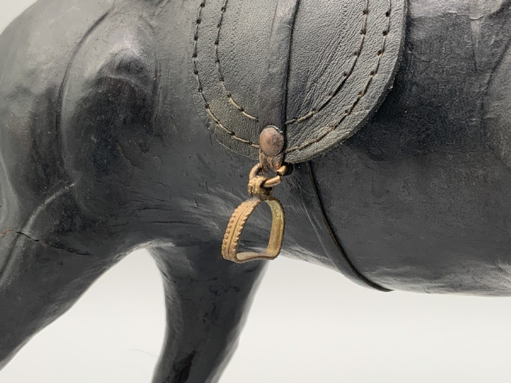 A standing vintage dark leather horse sculpture detailed with a miniature saddle, bridle, and metal stirrups. View XVII