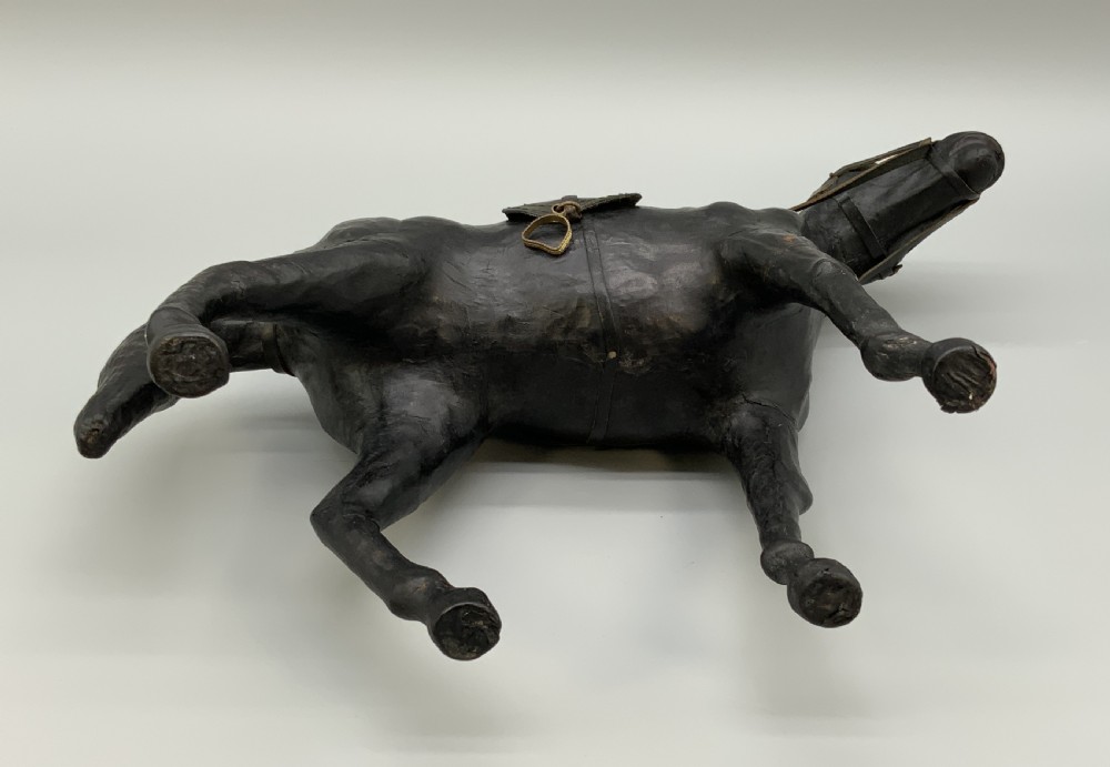 A standing vintage dark leather horse sculpture detailed with a miniature saddle, bridle, and metal stirrups. View XVIII