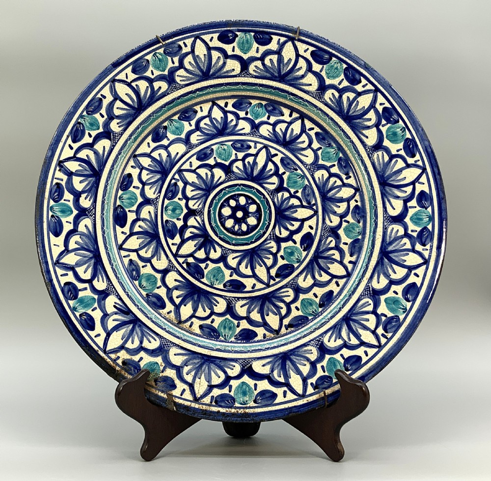 A large round tin-glazed earthenware charger plate featuring concentric hand-painted Moorish floral motifs in cobalt blue and turquoise on a cream ground.