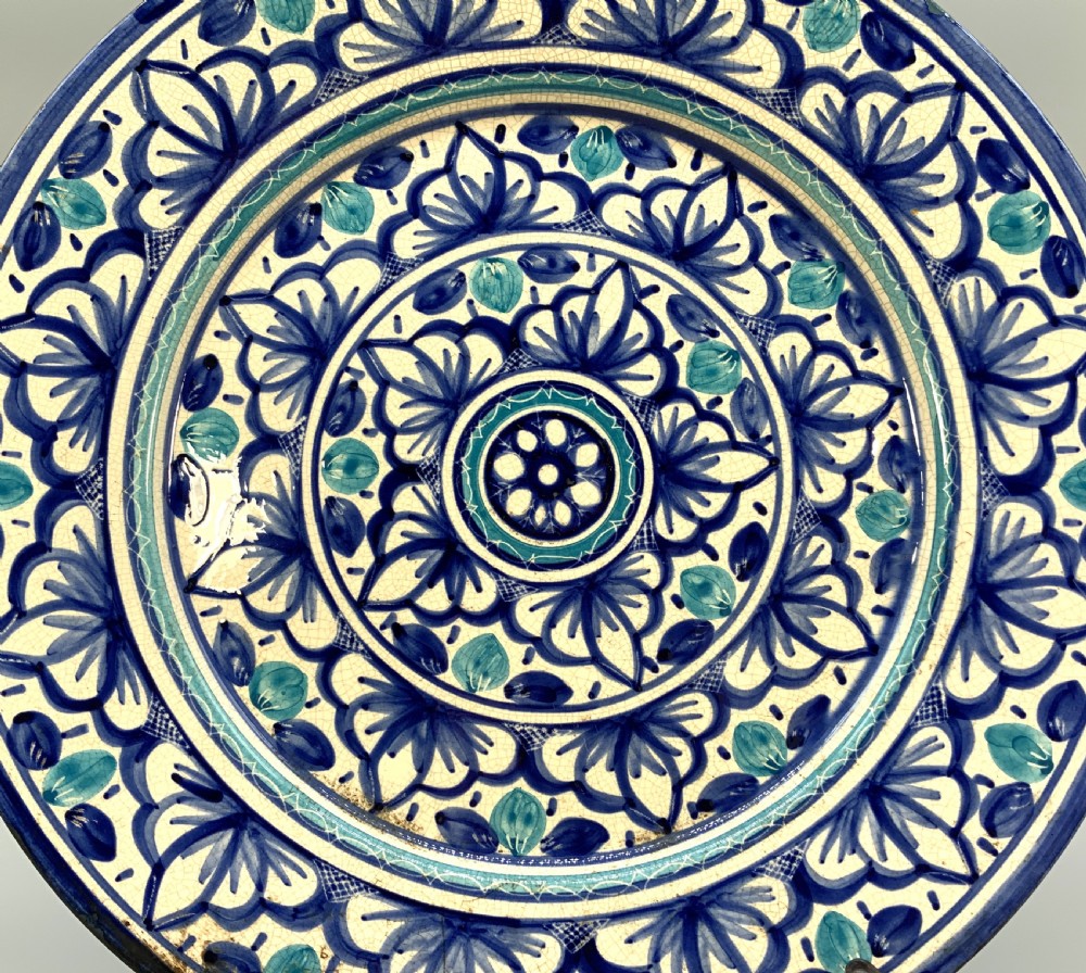 A large round tin-glazed earthenware charger plate featuring concentric hand-painted Moorish floral motifs in cobalt blue and turquoise on a cream ground. View IV