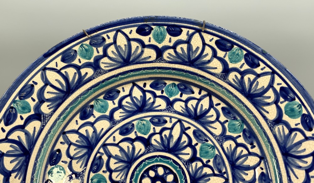 A large round tin-glazed earthenware charger plate featuring concentric hand-painted Moorish floral motifs in cobalt blue and turquoise on a cream ground. View V