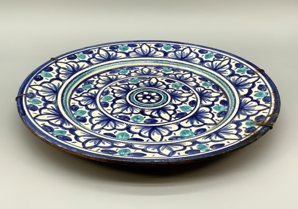 A large round tin-glazed earthenware charger plate featuring concentric hand-painted Moorish floral motifs in cobalt blue and turquoise on a cream ground. View XV