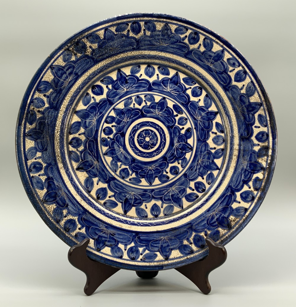 A circular blue and cream tin-glazed earthenware charger plate featuring hand-painted Moorish floral motifs and fine glaze crazing.