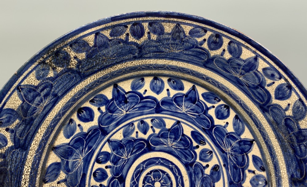 A circular blue and cream tin-glazed earthenware charger plate featuring hand-painted Moorish floral motifs and fine glaze crazing. View IV