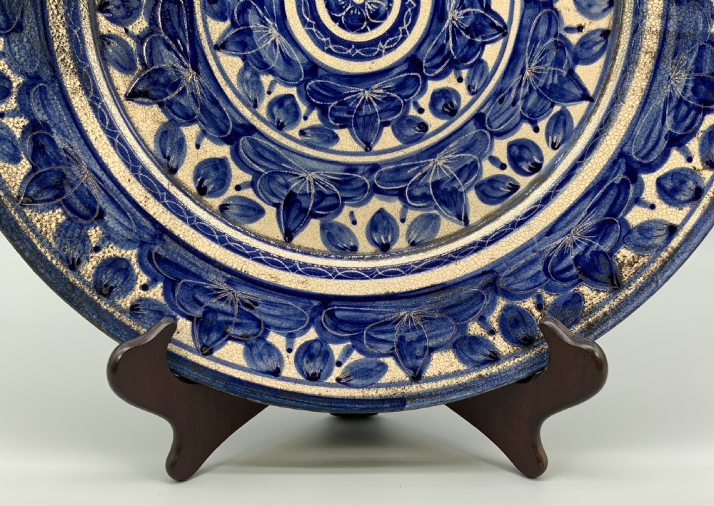 A circular blue and cream tin-glazed earthenware charger plate featuring hand-painted Moorish floral motifs and fine glaze crazing. View V