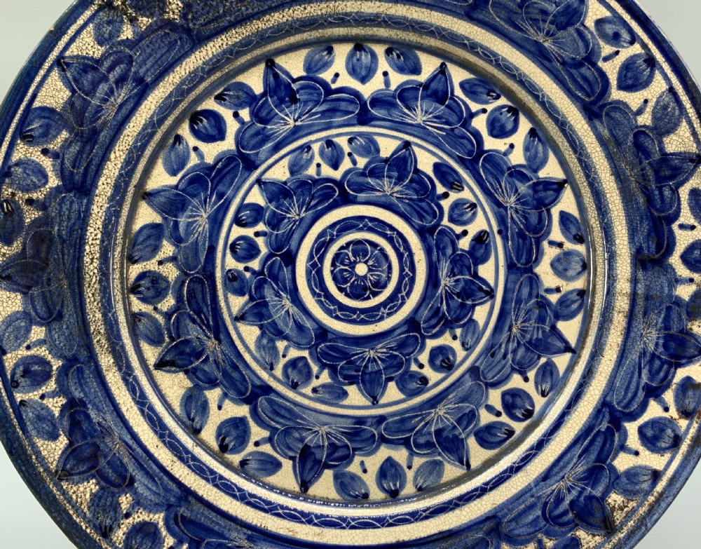 A circular blue and cream tin-glazed earthenware charger plate featuring hand-painted Moorish floral motifs and fine glaze crazing. View VIII