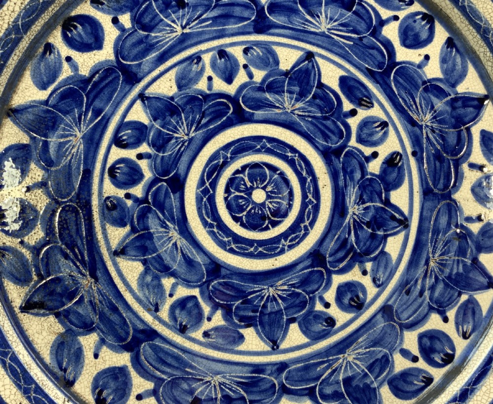 A circular blue and cream tin-glazed earthenware charger plate featuring hand-painted Moorish floral motifs and fine glaze crazing. View IX