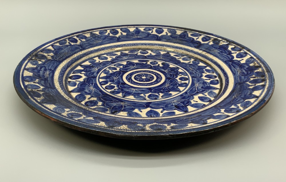 A circular blue and cream tin-glazed earthenware charger plate featuring hand-painted Moorish floral motifs and fine glaze crazing. View XIII
