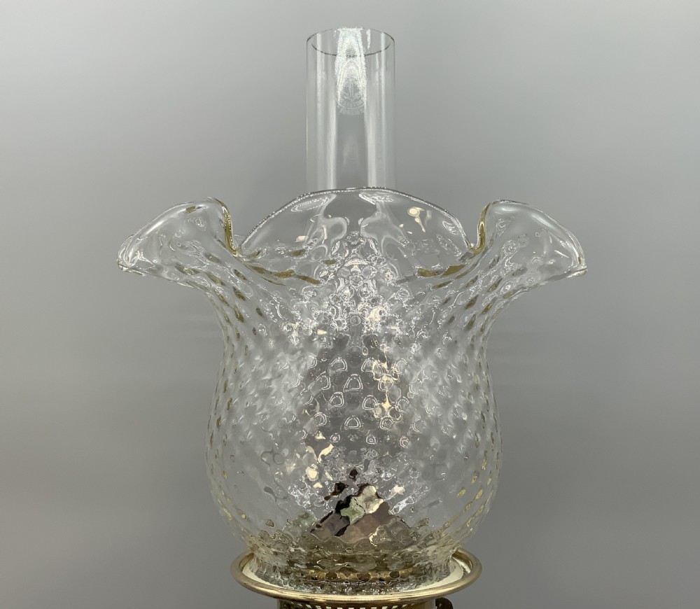 An Art Nouveau table oil lamp featuring a black ceramic base, cast brass stem, clear glass reservoir, double wick burner, clear chimney, and ruffled glass shade. View III